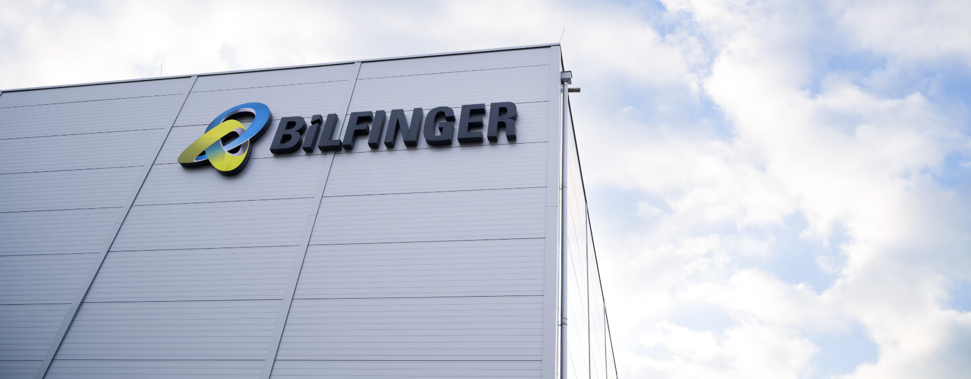 This image is a photograph of a building exterior prominently displaying the Bilfinger logo, emphasizing the company's branding and presence. The clear sky in the background adds a sense of openness and professionalism to the scene.
