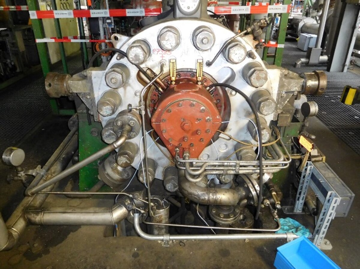 Front view of a turbocompressor with visible piping and mechanical components in an industrial setting.