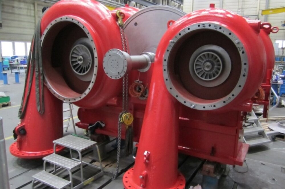 Large red turbo compressor unit with two visible rotors in an industrial workshop.