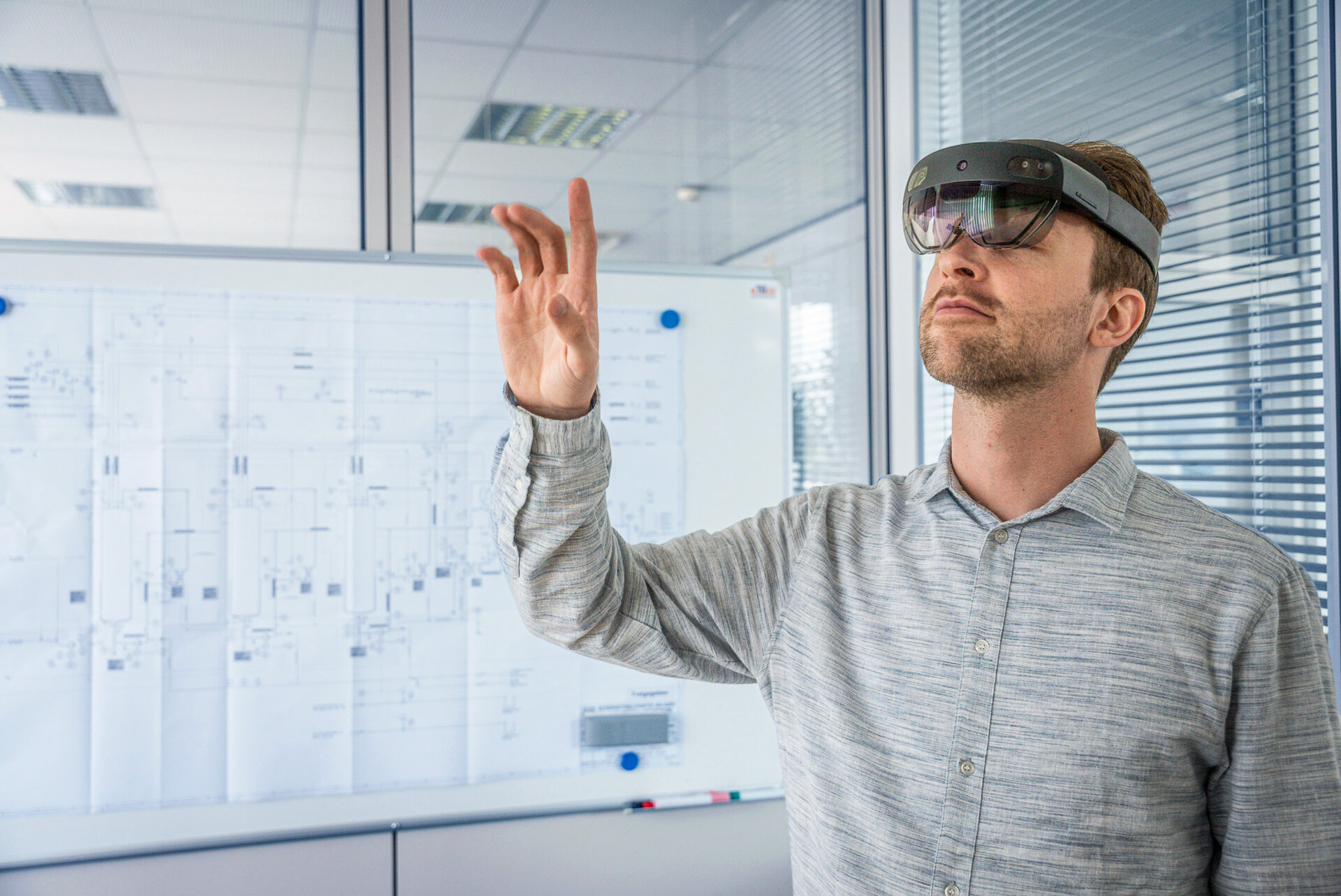 Reference_augmented Reality Person wearing a virtual reality headset interacting with virtual objects in a modern office with technical diagrams in the background.
