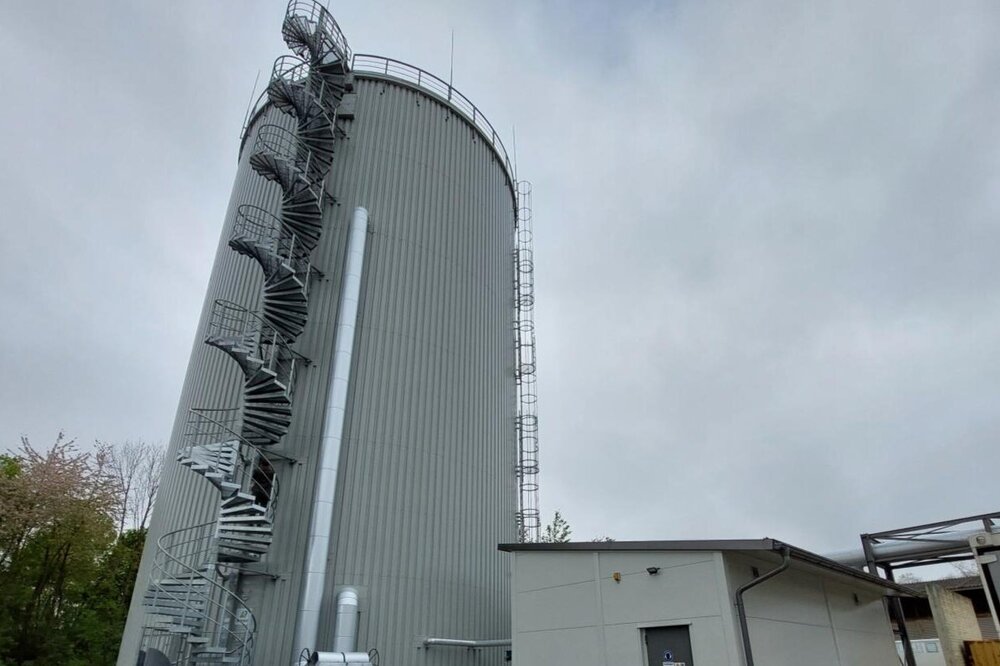 Large cylindrical district heating storage tank in Cologne with adjacent technical facilities and piping.