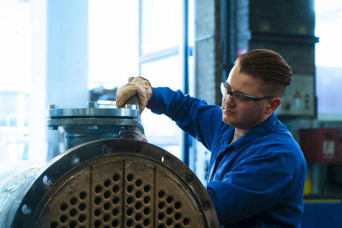 Bilfinger colleague repairs a tube heat exchanger for a customer in Frankfurt. The colleague is wearing an overall, gloves, safety goggles and hearing protection.